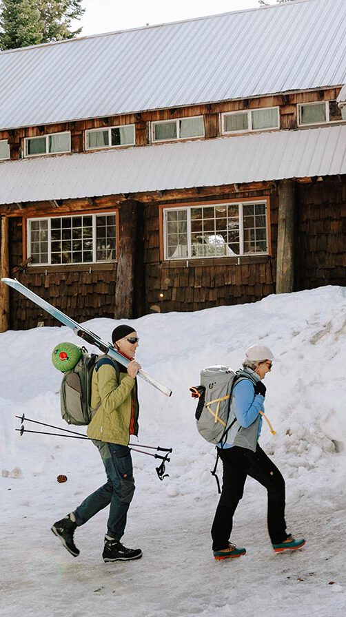 Two guests walking towards the lodge with ski equipment